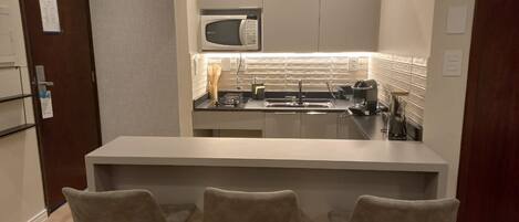 A compact kitchen with a microwave, stove, and modern pendant lights. There are three bar stools and a small island.
