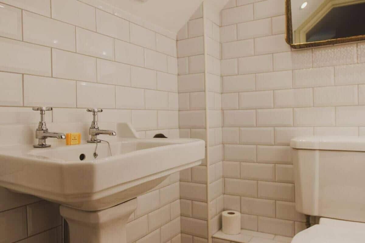 Un baño con azulejos blancos, un lavabo, un inodoro y un espejo.