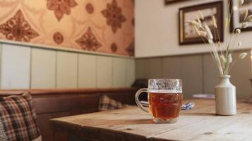 A wooden table with a glass mug of tea, a vase with dried plants, and a patterned wall in the background.
