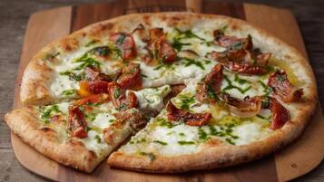 A pizza with cheese, bacon, and herbs on a wooden board.