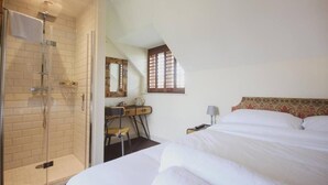 Un dormitorio con cama, escritorio, silla, ducha y ventana.