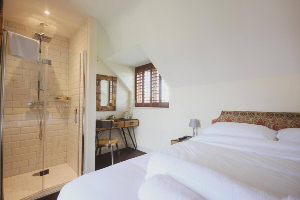 A bedroom with a bed, a desk, a chair, a shower, and a window.
