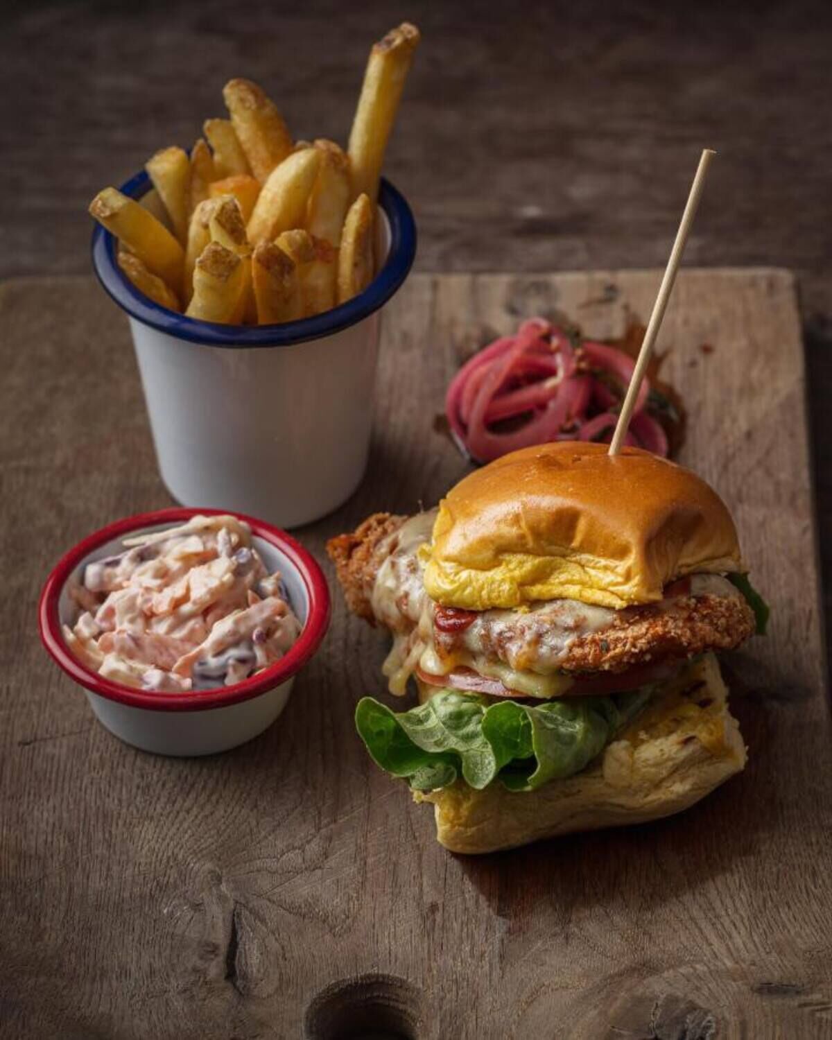 Una comida que incluye una hamburguesa con carne frita, papas fritas y un pequeño bol de ensalada de col.