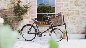 Una bicicleta con canasta y un letrero que dice "The Bell" estacionada frente a un edificio de piedra con ventana.