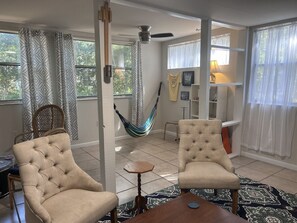 A spacious living room with two beige armchairs, a hammock, and a small round table.