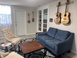 A living room with a blue sofa, a beige armchair, a wooden coffee table, and two guitars on the wall.