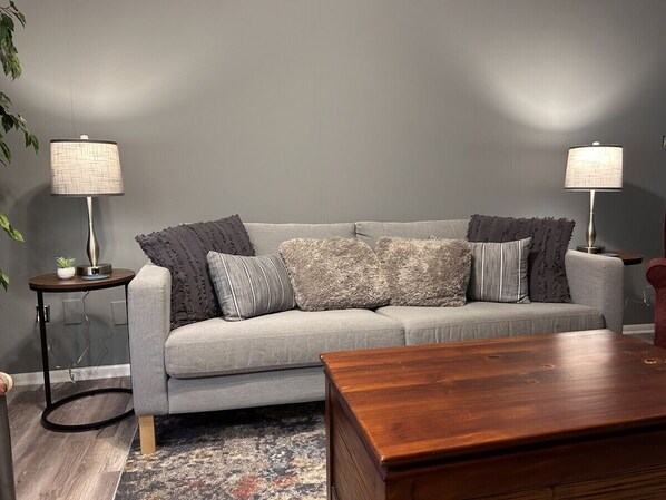 A modern living room with a grey sofa, two side tables with lamps, and a wooden coffee table.