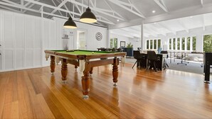 Amplia habitación con mesa de billar, piso de madera y techo alto con vigas a la vista.