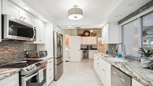 A modern kitchen with stainless steel appliances, white cabinetry, and a marble countertop.