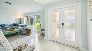 A spacious living room with a grey sofa, a green coffee table, and a white armchair.