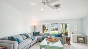 A spacious living room with a grey sectional sofa, a green coffee table, and a white console table with a vase.