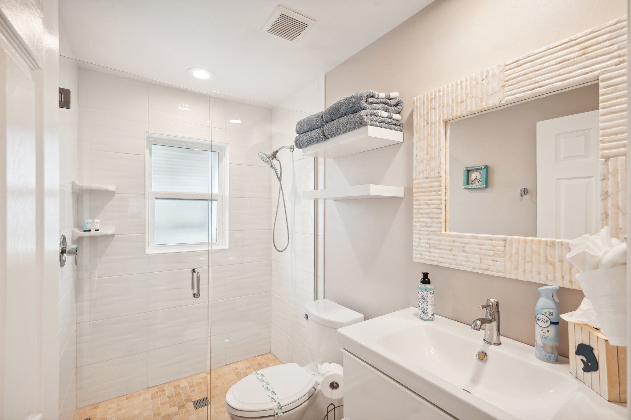 Une salle de bain moderne avec une douche à parois de verre, des toilettes, un lavabo avec un miroir et une fenêtre.