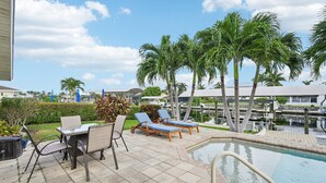 An outdoor pool area with lounge chairs, a table, and palm trees.