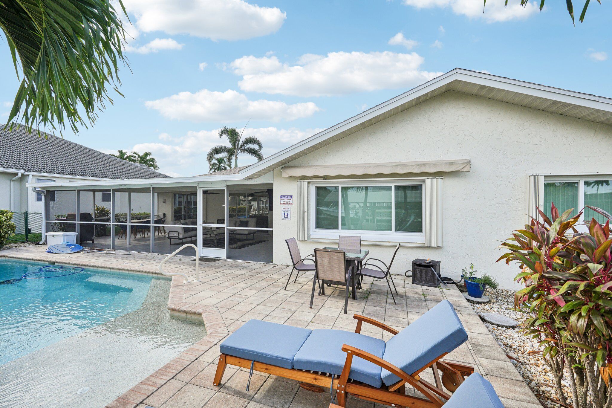 A poolside area with lounge chairs, a covered patio, and a view of the pool.