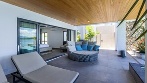 A modern outdoor living area with a wooden ceiling, a circular seating area with cushions, and a glass door leading to a pool. - Trilogy Villas Denarau (Nadi)