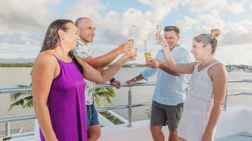 A group of people toasting on a boat with a view of the water and palm trees in the background.