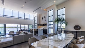 A spacious living area with a large marble table, comfortable seating, a kitchen area, and large windows offering a view of the water. - Trilogy Villas Denarau (Nadi)