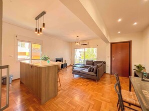 Un amplio salón con suelo de parqué laberíntico, una isla central con lavamanos, un sofá y una mesa de comedor.