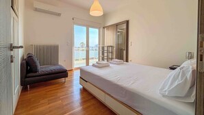 A bedroom with a bed, a dark sofa, a radiator, a ceiling light, and a view through a sliding door. - Light & Ample Flat near Glyfada Center (Glifada)