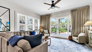 A spacious living room with a beige sofa, a blue patterned rug, and a ceiling fan.