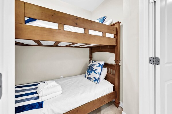A bunk bed with a wooden frame, white bedding, and a blue and white striped blanket.
