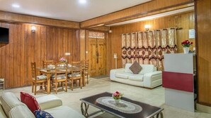 A living room with a wooden wall, a dining table with chairs, a sofa, and a coffee table. - Oak View shimla (Shimla)