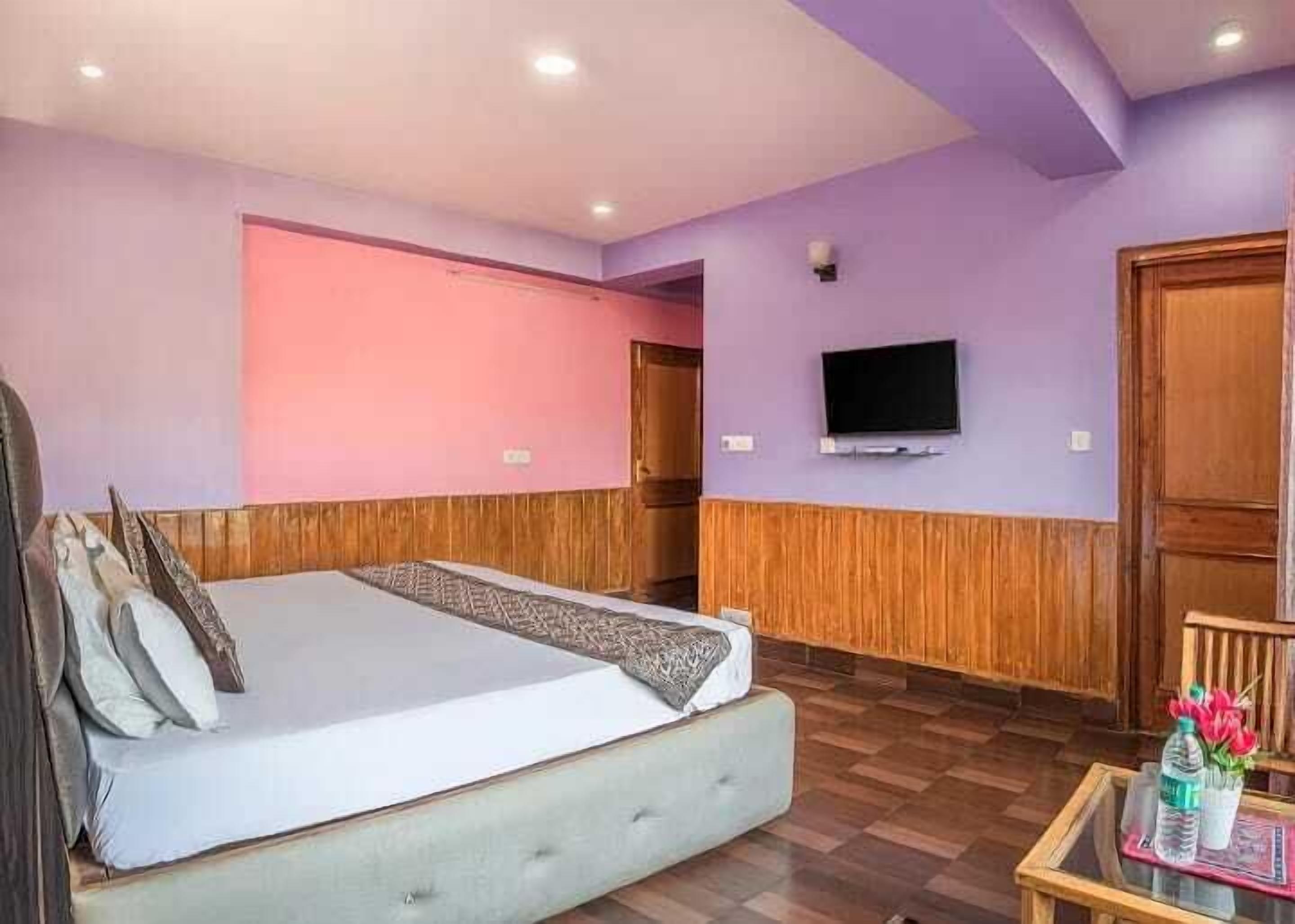 A hotel room with a bed, a television, and a wooden floor.
