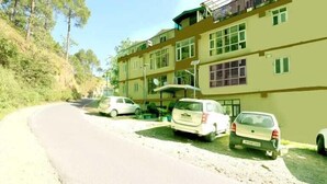 A multi-story building with a parking area in front. - Oak View shimla (Shimla)