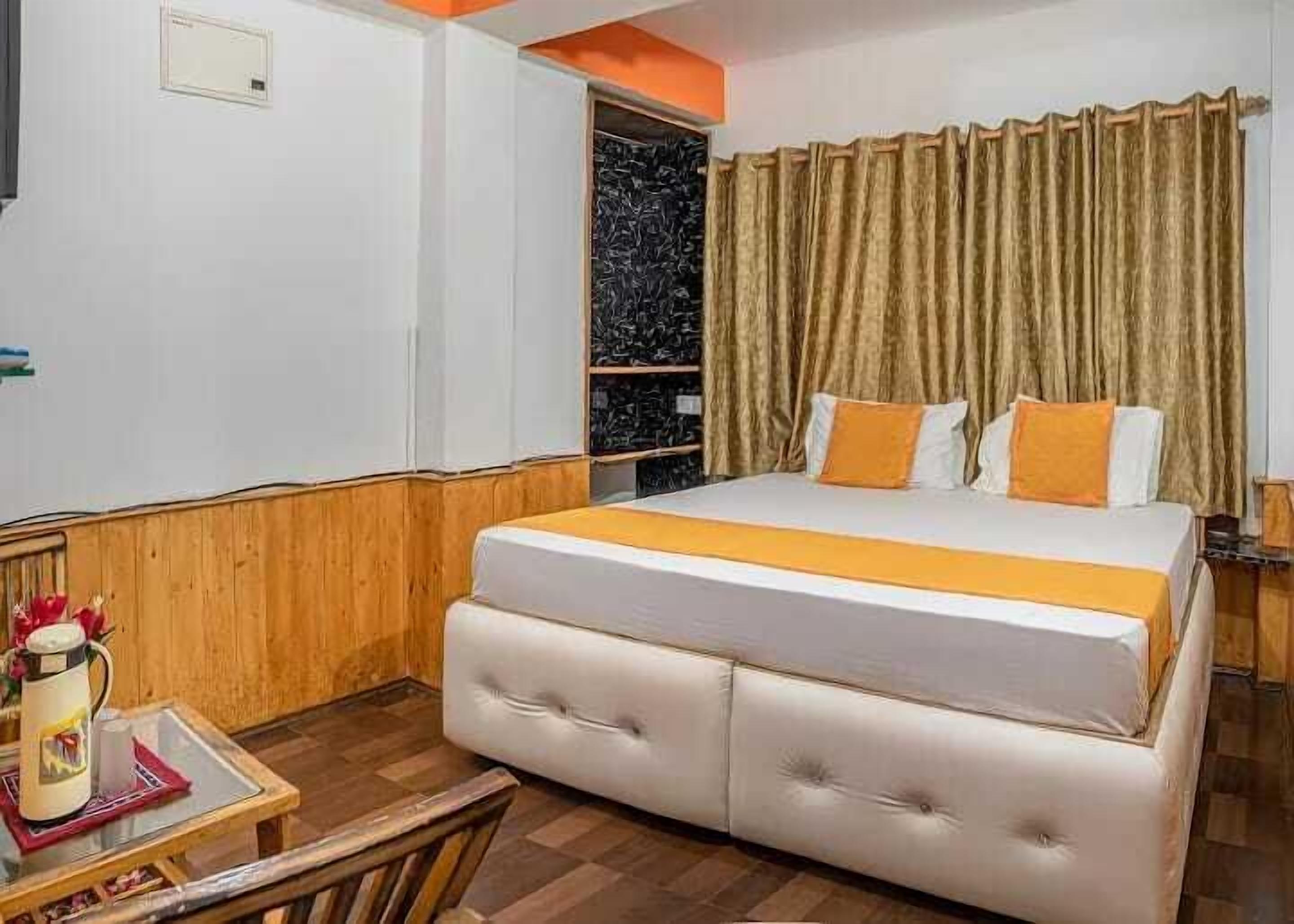 A hotel room with a large bed, a wooden side table with a pitcher, and a small table with a cup and saucer.