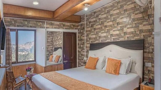 A bedroom with a large bed, wooden headboard, and a view of a cityscape through a window. - Oak View shimla (Shimla)