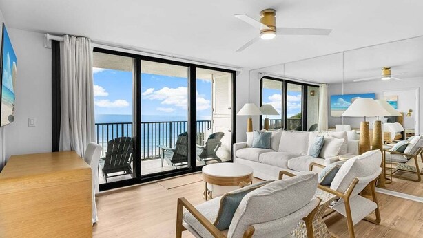 Un vaste espace de vie avec un balcon donnant sur la mer, aménagé avec un canapé, des fauteuils et une table en bois.