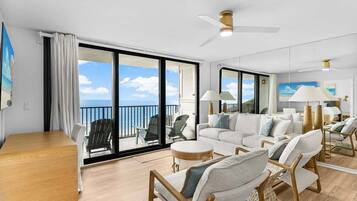 Un vaste espace de vie avec un balcon donnant sur la mer, aménagé avec un canapé, des fauteuils et une table en bois.