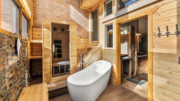 A wooden cabin interior with a large bathtub, a wooden bench, and a brick wall.