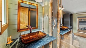 A bathroom with a wooden vanity, a copper vessel sink, and a large mirror.