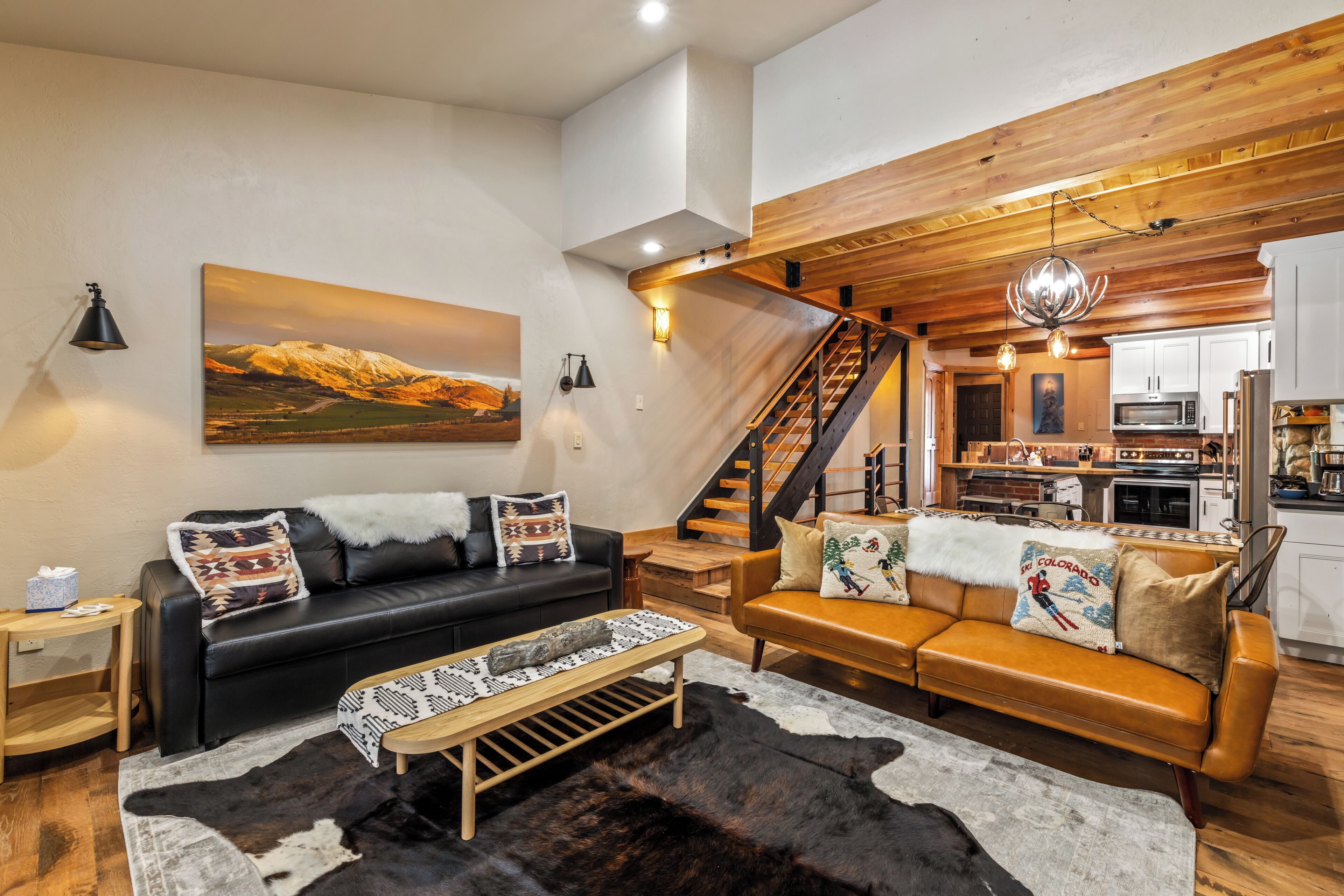 Ein modernes Wohnzimmer mit einer schwarzen Ledersofa, einem Holztisch und einem großen Gemälde einer Berglandschaft.
