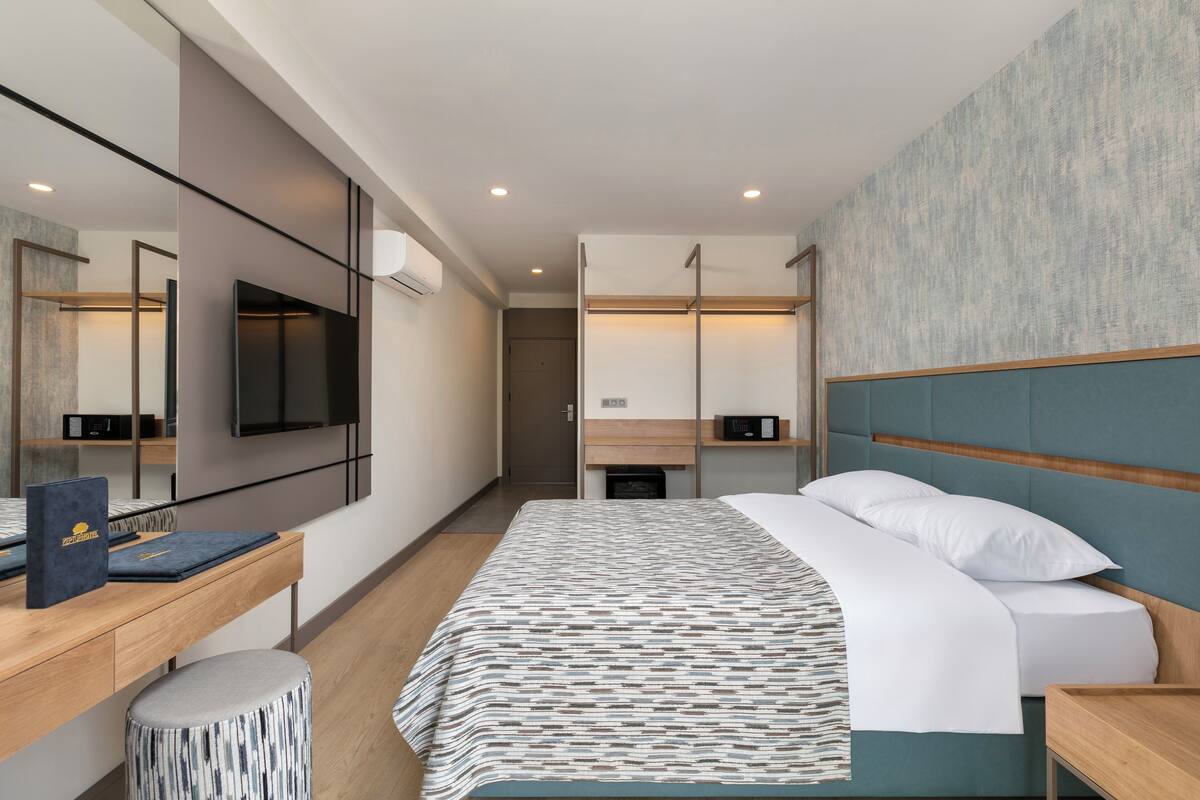 Una camera d'albergo moderna con un letto grande, una scrivania con un computer, una TV e un ampio specchio.