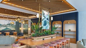 A modern lounge area with a wooden table surrounded by chairs, a large plant centerpiece, and a mural on the wall. - Keptur Hotel (Dosemealti)