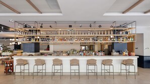 A bar area with multiple shelves of bottles, a counter with bar stools, and a seating area with chairs. - Keptur Hotel (Dosemealti)