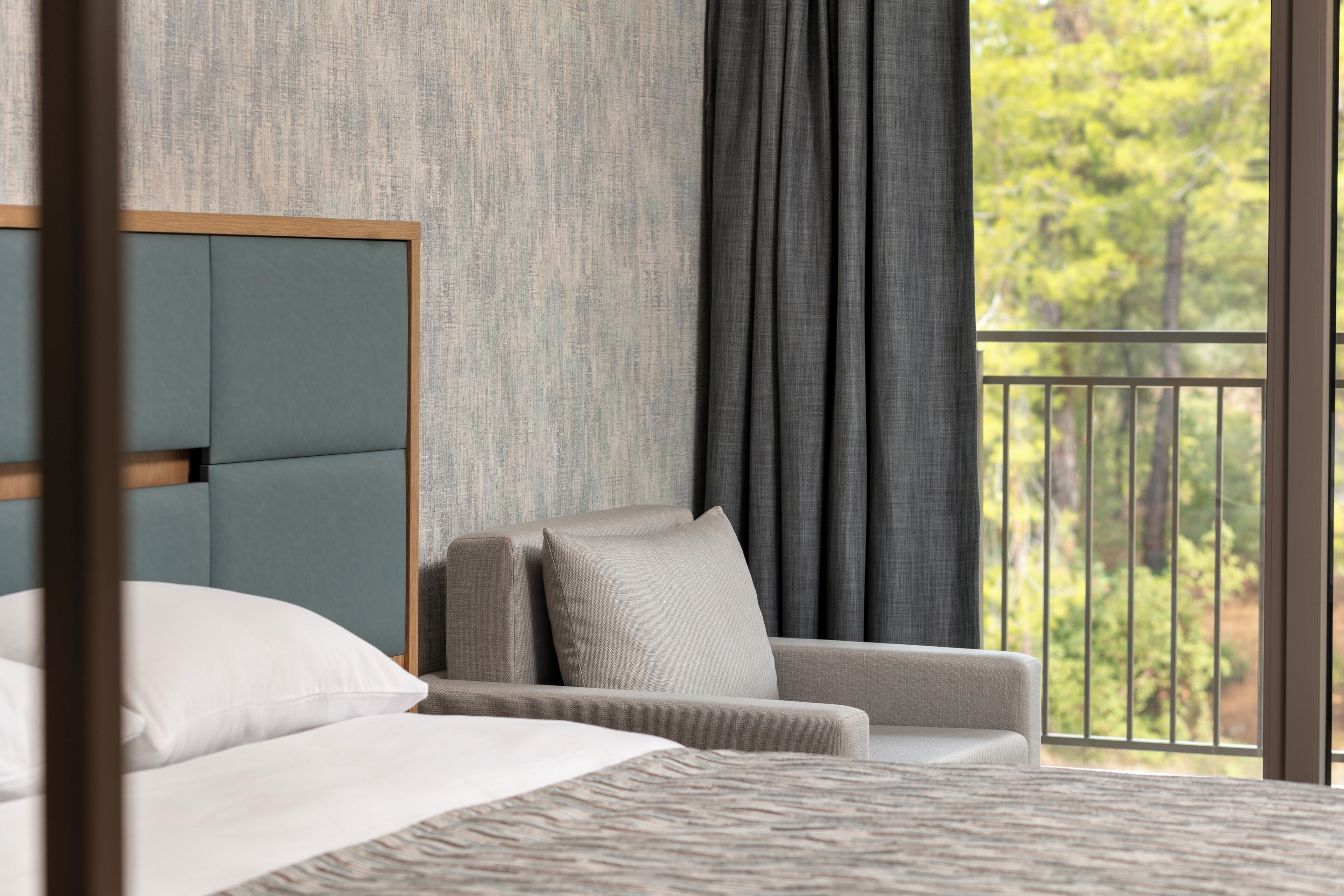 A modern hotel room with a large bed, a sofa, and a view of trees through the window.