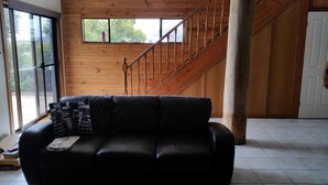 A room with a black leather sofa, a wooden staircase, and a large window. - Woodstock 3 Francis St, Port Elliot (Port Elliot)