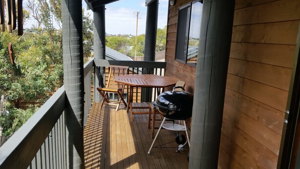 A wooden deck with a table and chairs, a grill, and a view of greenery. - Woodstock 3 Francis St, Port Elliot (Port Elliot)