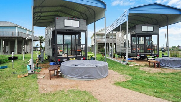 Uma casa móvel moderna estilo RV com área externa coberta, um pequeno deck e um espaço de estar circular.