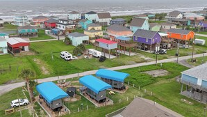 Vista aérea de uma área residencial costeira com casas coloridas, uma estrada e uma praia ao fundo.