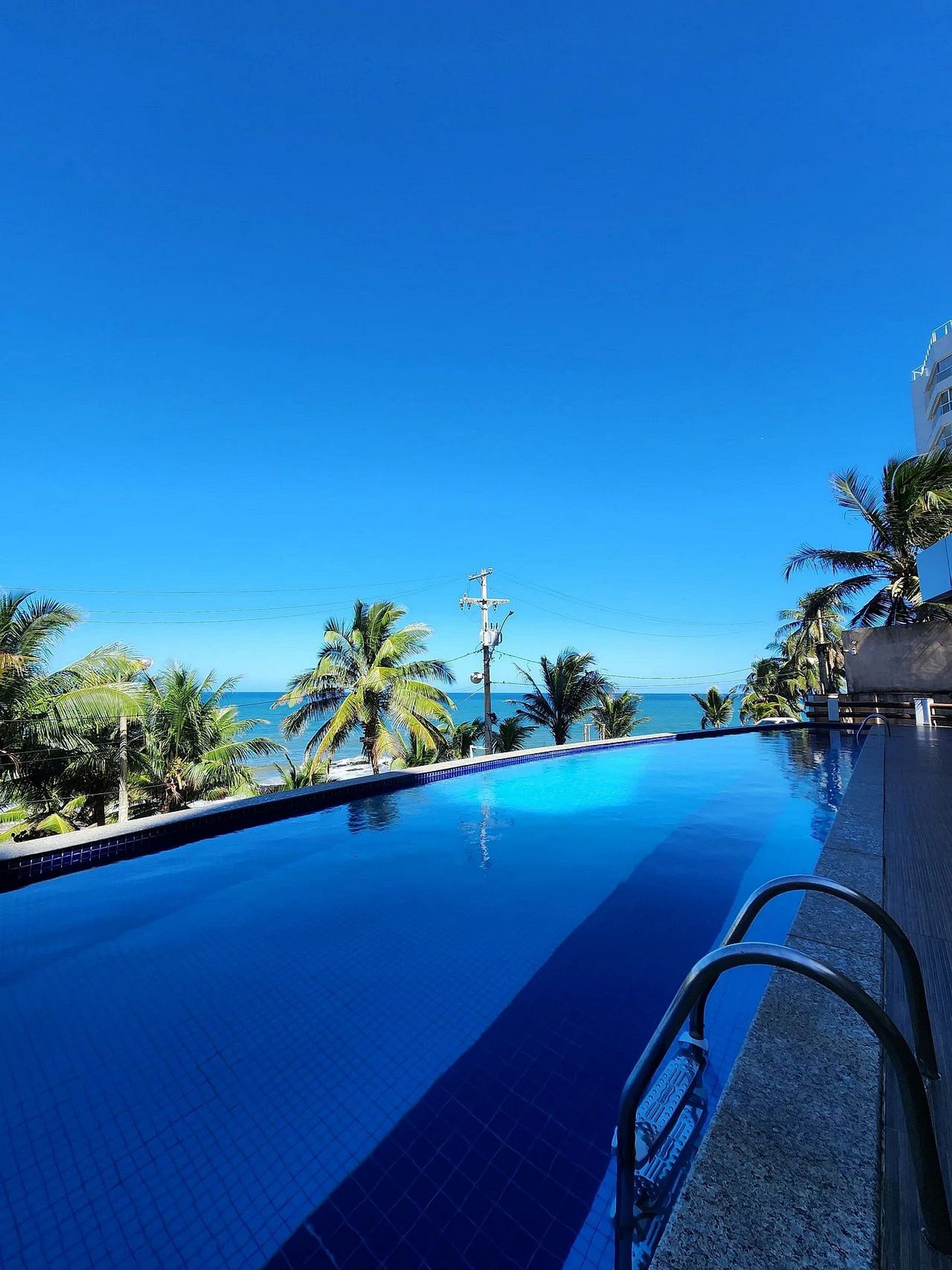 Una piscina blava i cristal·lina amb vista a l'oceà, envoltada de palmeres i un edifici.