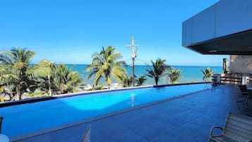 Zona junto a la piscina con vistas al océano, sillas de descanso y un edificio moderno.