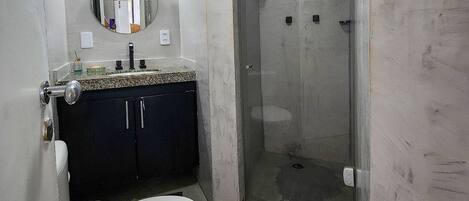 A bathroom with a toilet, sink, mirror, and shower.