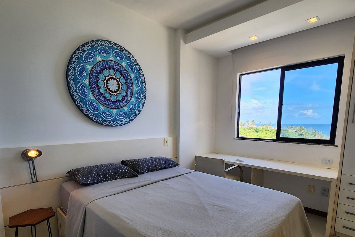 Quarto moderno com uma cama grande, uma escrivaninha e uma janela com vista.