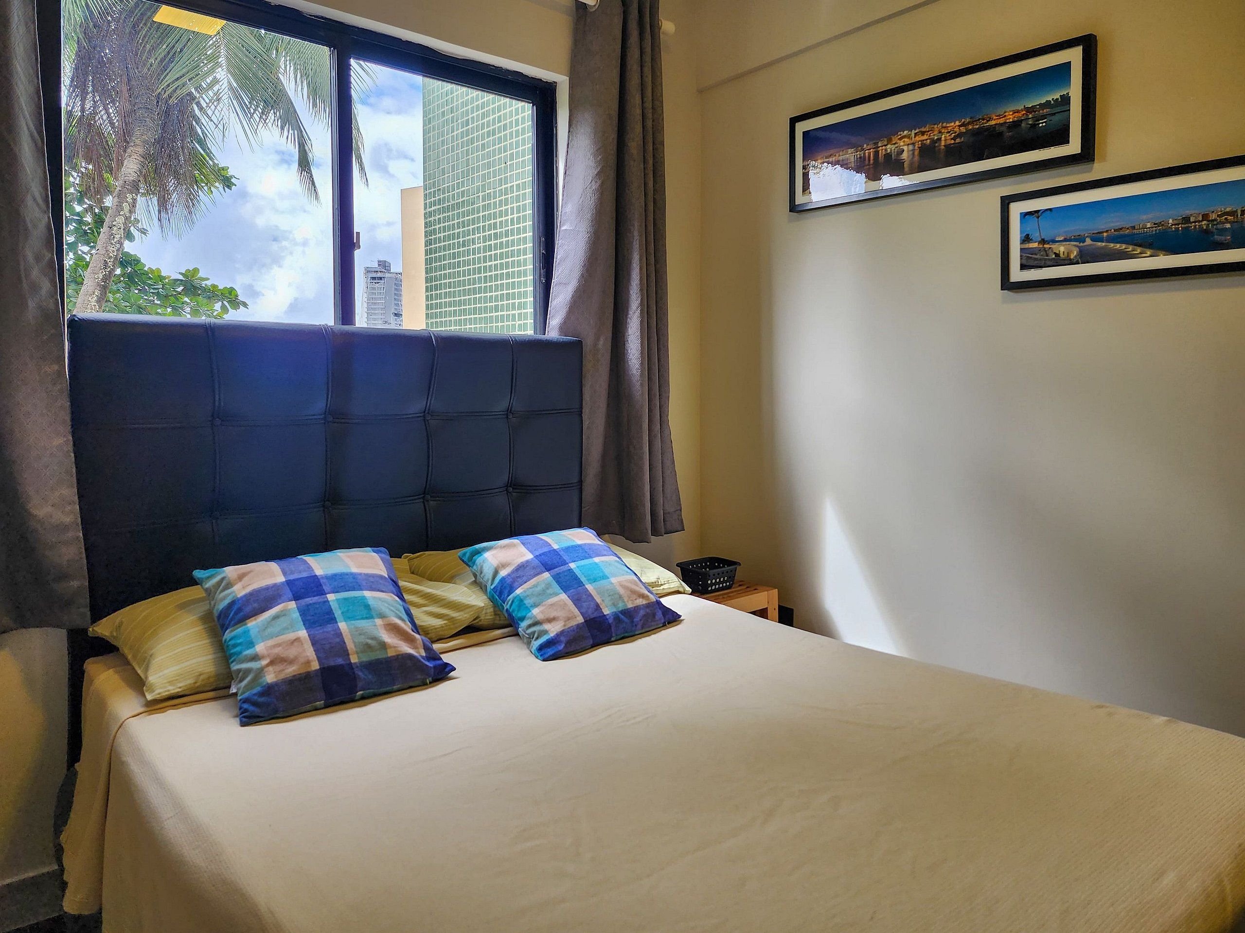 Ein Schlafzimmer mit einem Bett, zwei Kissen, einem Fenster mit Vorhängen und zwei gerahmten Bildern an der Wand.