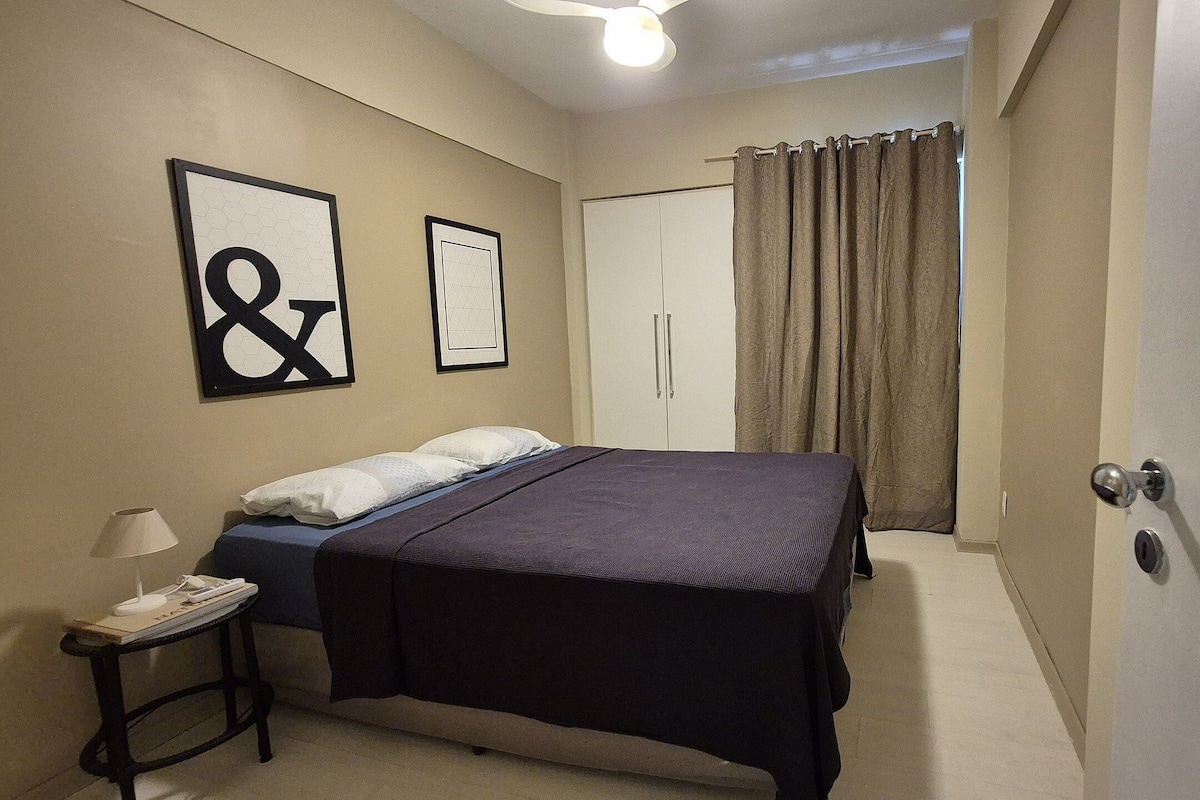 Quarto com cama, mesa de cabeceira, abajur e porta.