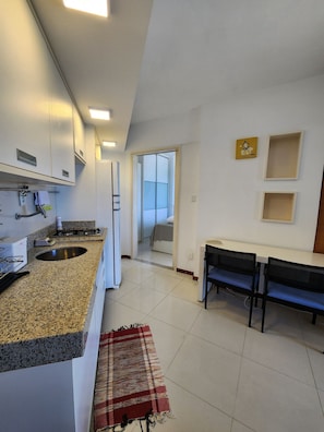 A modern kitchen with granite countertops, a built-in oven, and a dining area with a bench and table. - Sol Nascente (Salvador)